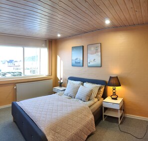 A bedroom with a bed, a nightstand, a lamp, and two wall-mounted pictures.