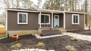 A single-story house with a front porch, a door, and a small garden area with mulch and stepping stones. - Renovated Raleigh Bungalow (Raleigh)