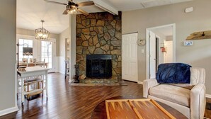 A living room with a stone fireplace, a ceiling fan, and a dining area with a kitchen in the background. - Renovated Raleigh Bungalow (Raleigh)