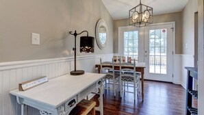 A dining area with a white table, chairs, a chandelier, and a large window. - Renovated Raleigh Bungalow (Raleigh)
