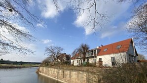 Ein Haus am Flussufer mit Betonbefestigung, einem roten Dach und einer Brücke im Hintergrund.