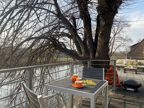 A deck with a table set for two, overlooking a body of water and a tree. - Luxus Loft im Schleusenhaus auf der Insel in Hameln (Hameln)