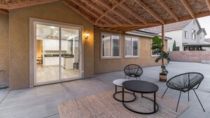 Un patio exterior con una pérgola de madera, una mesa de comedor con dos sillas y una planta en maceta.