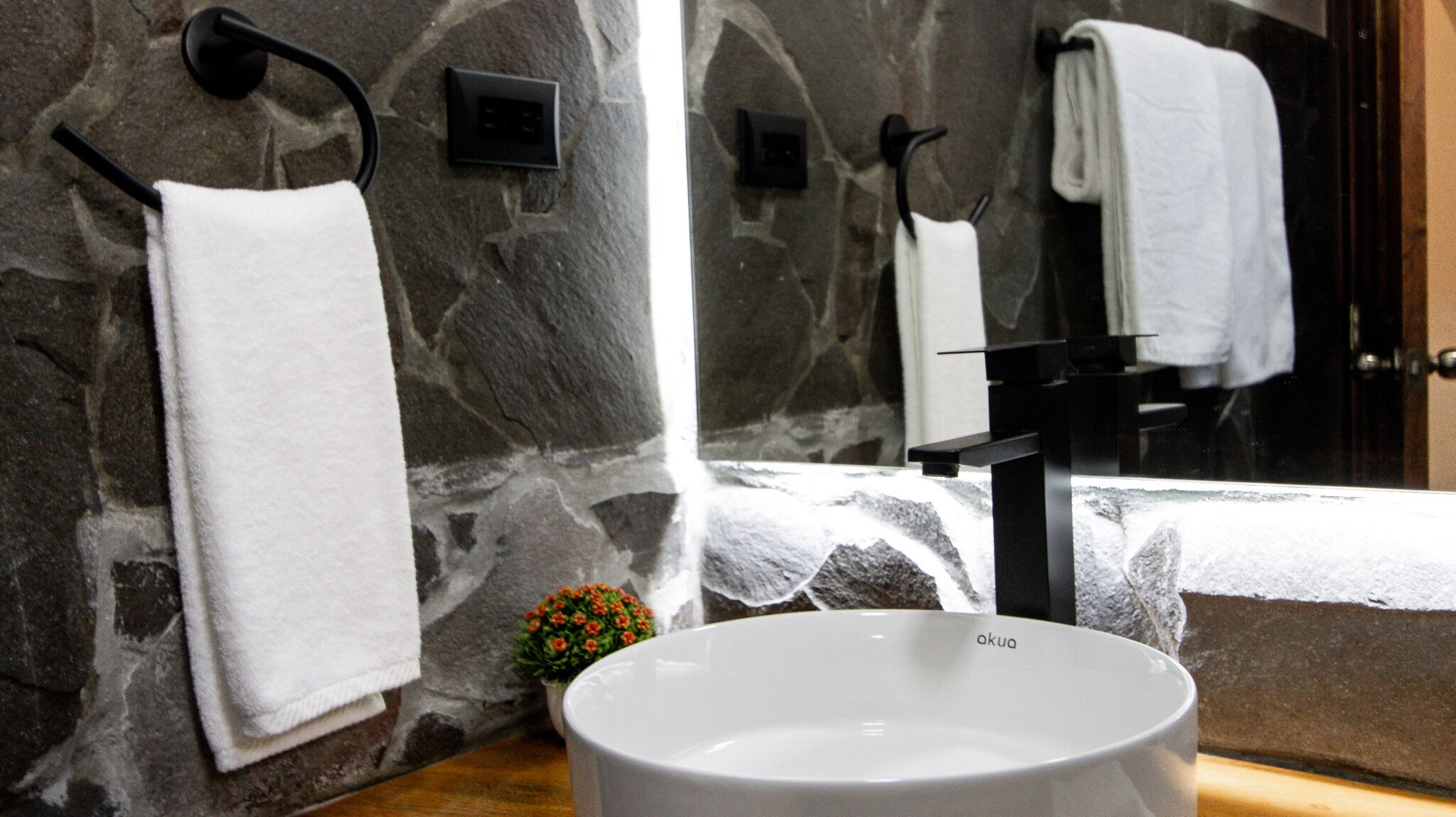 A bathroom with a stone wall, a white sink, and two towels hanging on black towel hooks.
