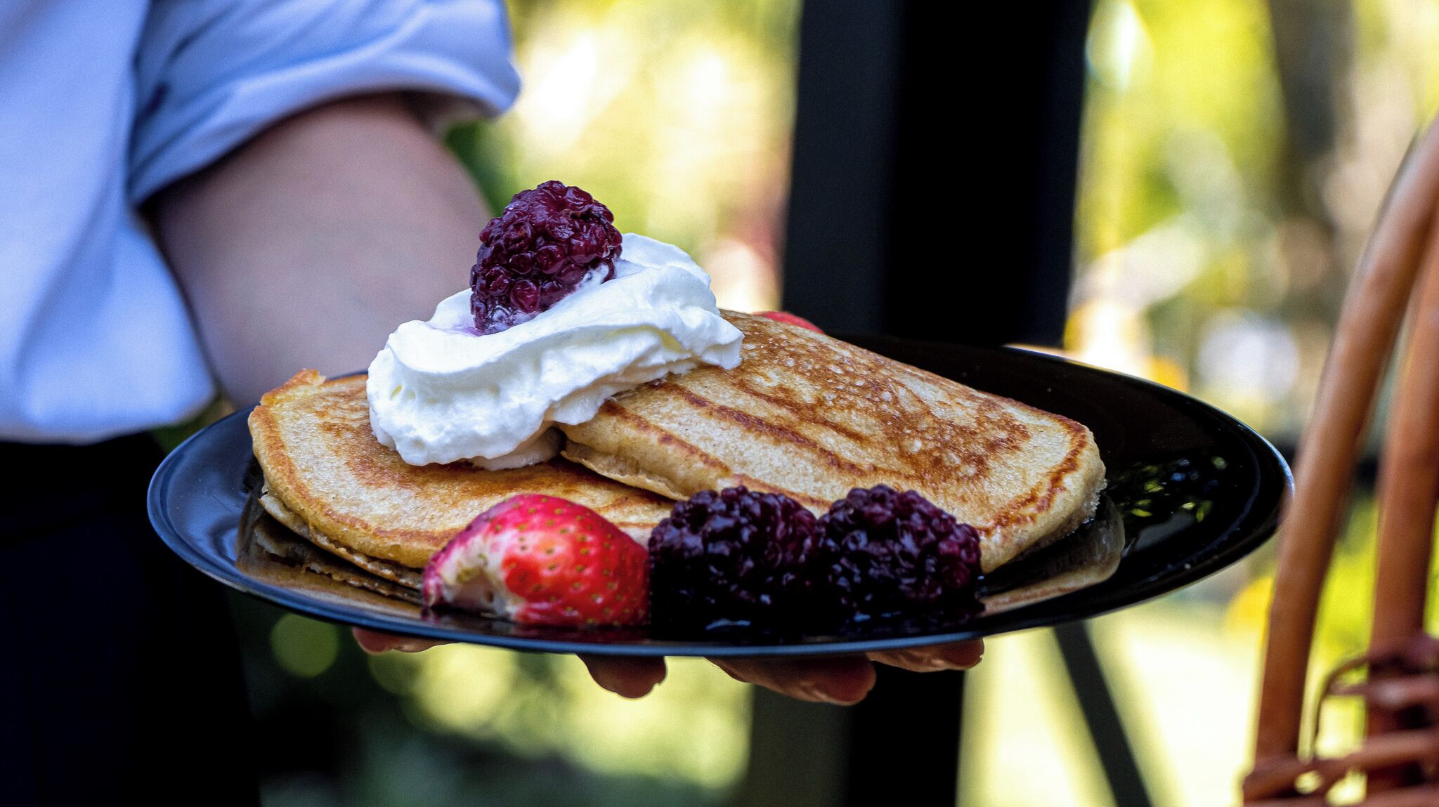 Un plato con dos tortitas, crema batida, una fresa y moras.