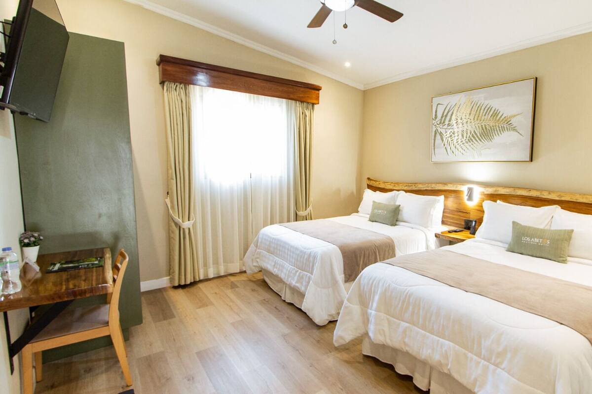 Une chambre d’hôtel avec deux lits, un bureau, une chaise, une télévision et un ventilateur de plafond.