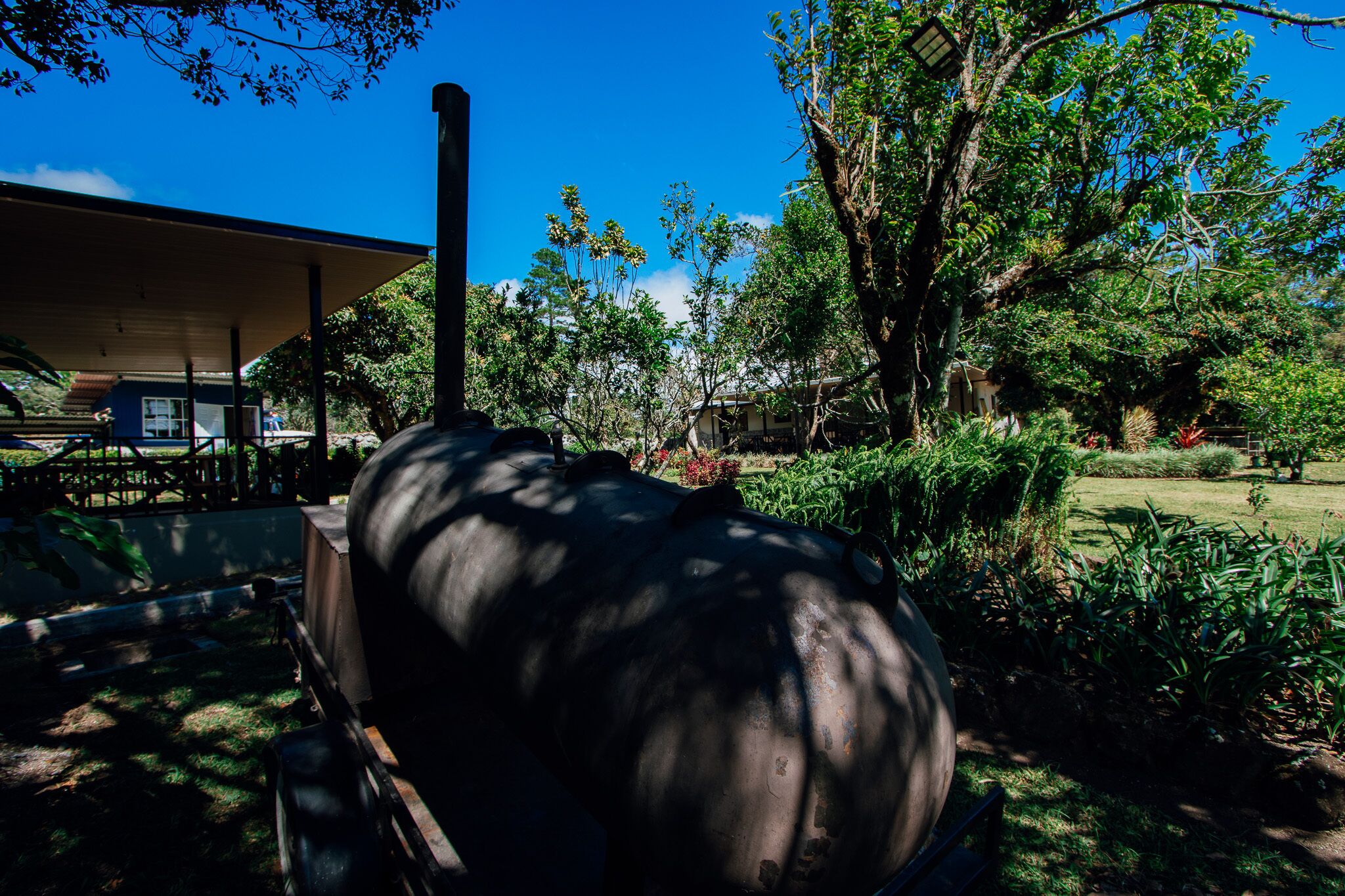 A large cylindrical structure, possibly a water tank, in a garden with trees and a building in the background.