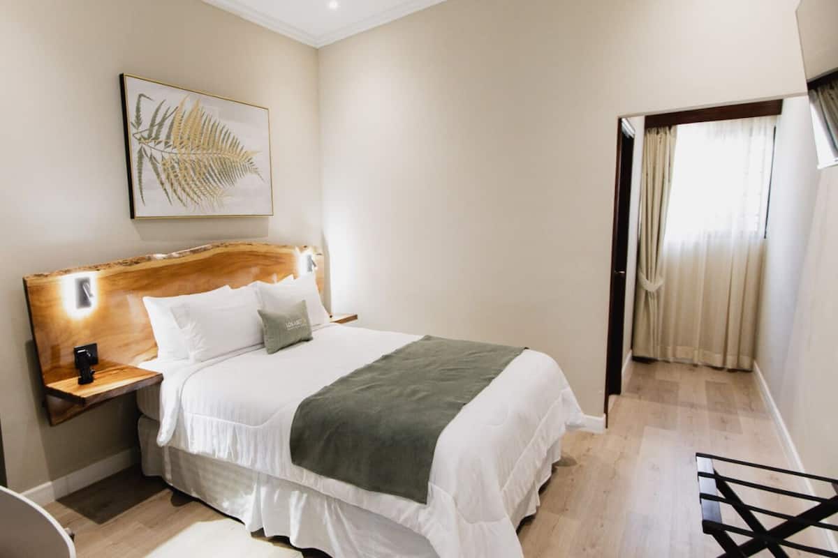 Un lit bien fait, avec une tête de lit en bois, une table de chevet avec une lampe et une grande fenêtre avec des rideaux.