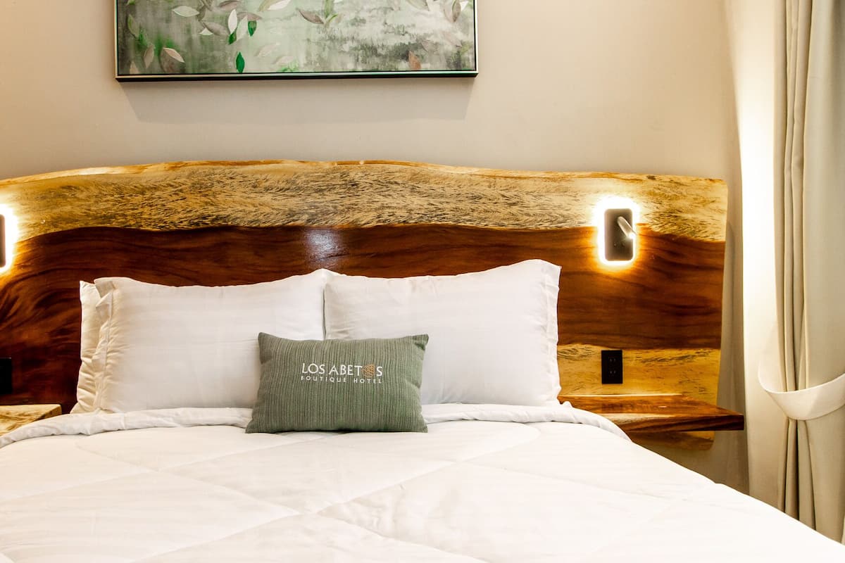 Un lit avec une tête de lit en bois, deux oreillers blancs et un oreiller vert avec du texte.
