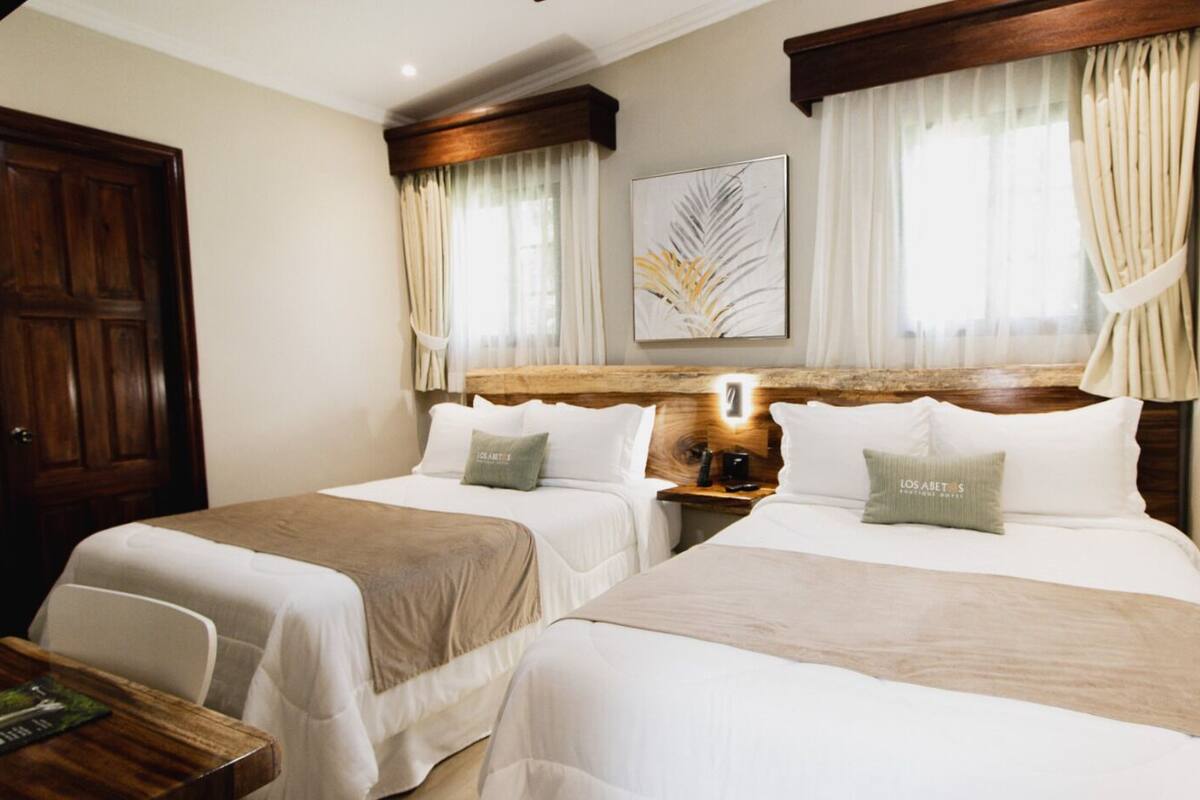 Une chambre d’hôtel avec deux lits, une tête de lit en bois, une table de chevet et une œuvre d’art encadrée au mur.