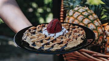 A waffle with whipped cream and a strawberry on a black plate.