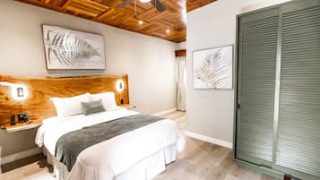Een slaapkamer met een houten hoofdbord, een bed met witte lakens, een grijze plaid en twee kunstwerken met bladeren in lijsten aan de muur.