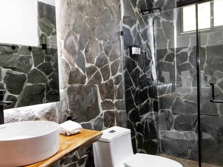 A bathroom with a stone wall, a round sink, a toilet, and a glass shower enclosure.