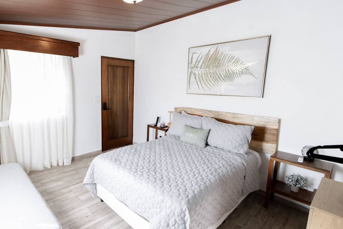 Une chambre à coucher comprenant un lit, une table de chevet, une commode, une fenêtre avec des rideaux et une porte.