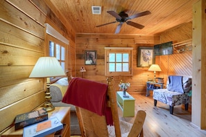 A cozy cabin interior with wooden walls, a ceiling fan, a bed, a chair, a table, and a lamp. - Bison Hollow Hideaway (South Bloomingville)