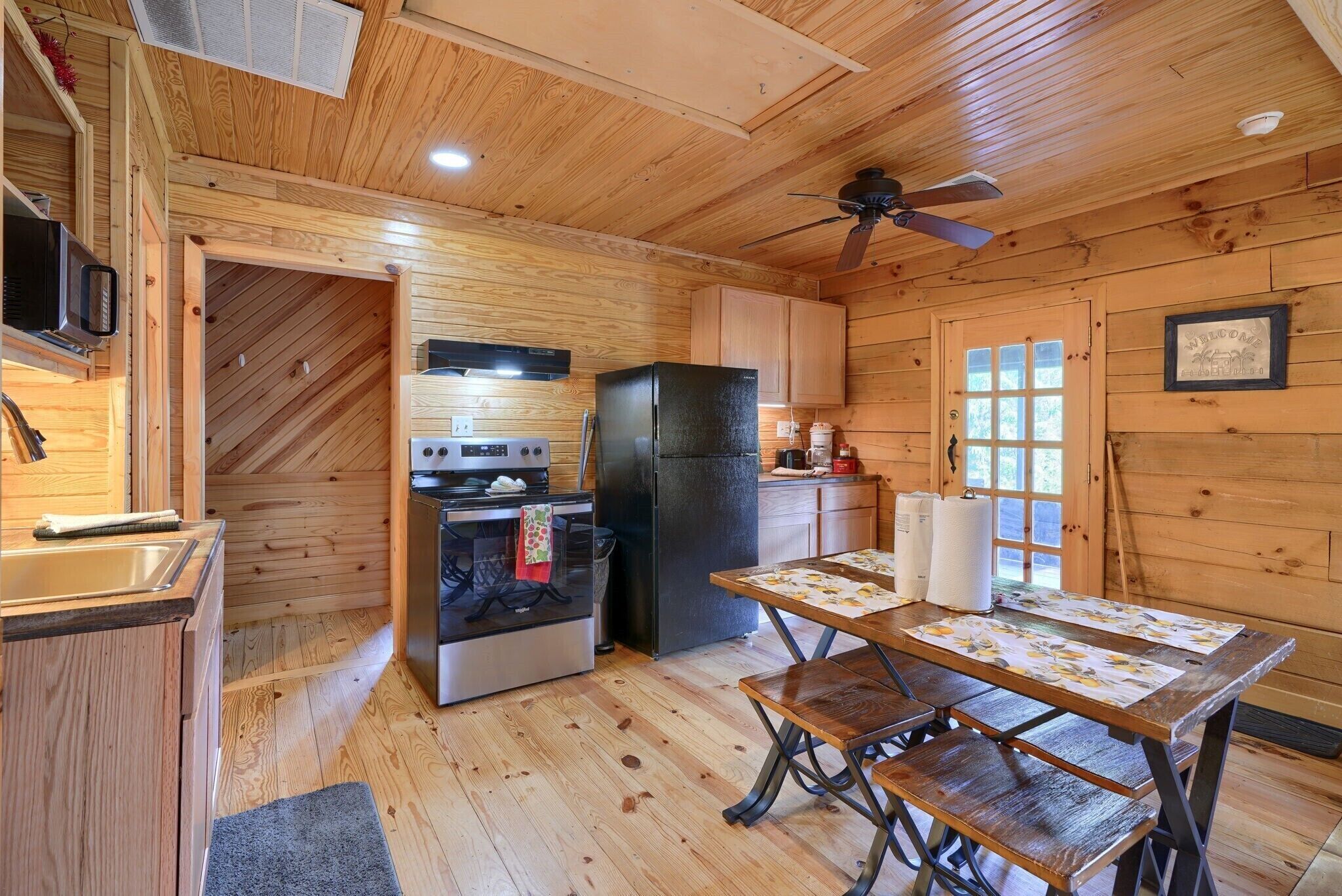 A cozy cabin-style kitchen with wooden walls, a black refrigerator, a stove, and a dining table set for four.