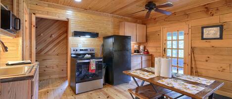A cozy cabin-style kitchen with wooden walls, a black refrigerator, a stove, and a dining table set for four.