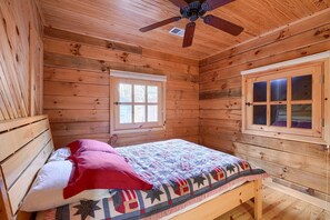 A wooden cabin bedroom with a bed, a window, and a ceiling fan. - Bison Hollow Hideaway (South Bloomingville)
