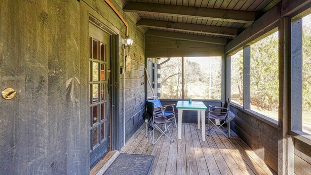 Une véranda couverte avec une table et des chaises en bois, une fenêtre et une porte.