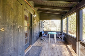 Une véranda couverte avec une table et des chaises en bois, une fenêtre et une porte.