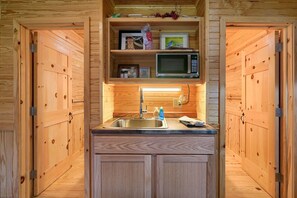Eine kleine Küche mit Holzausbau, einem Edelstahlspülbecken und einer Mikrowelle auf einer Ablagefläche.