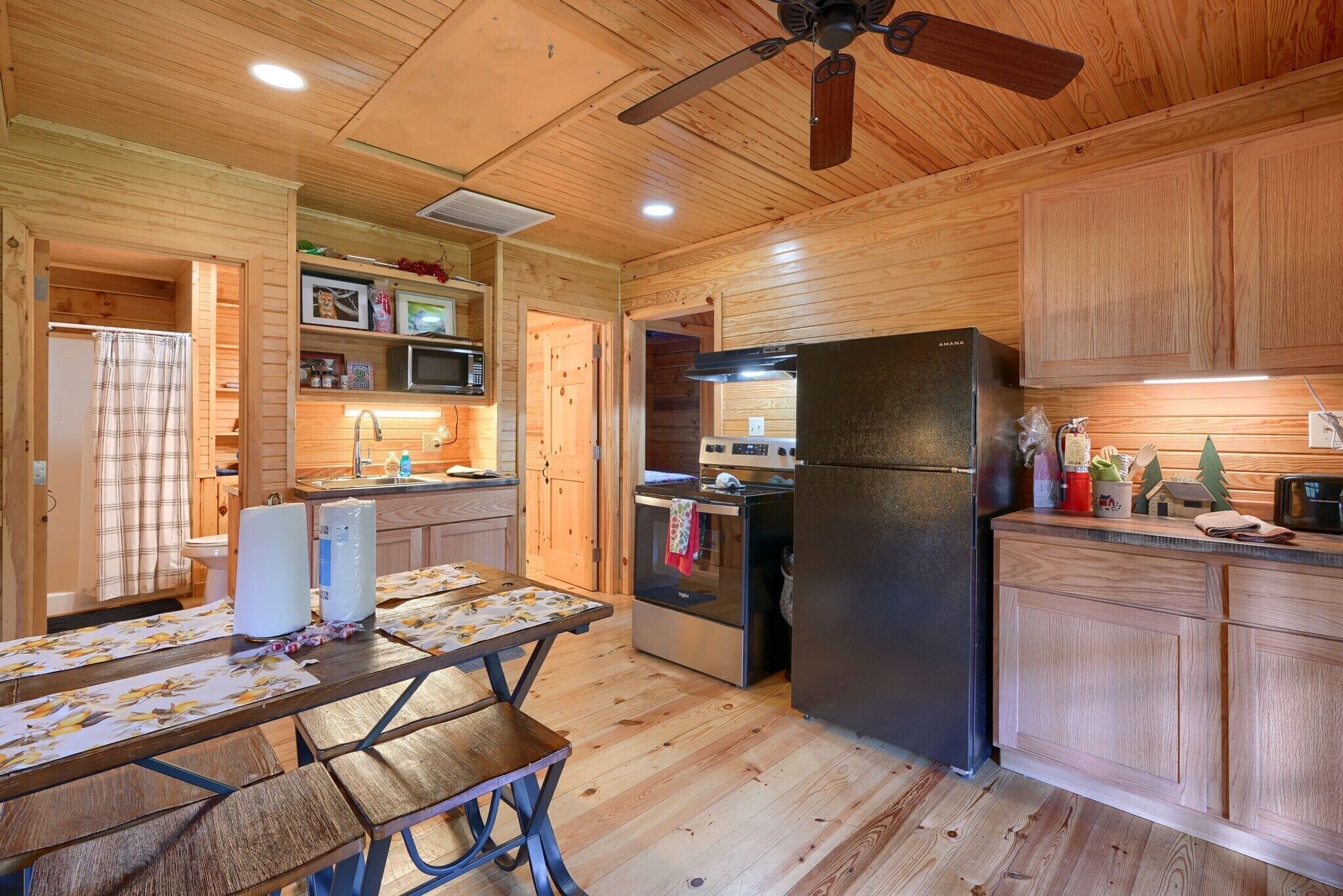 A wooden cabin interior with a kitchen area featuring a refrigerator, oven, microwave, and wooden cabinets.