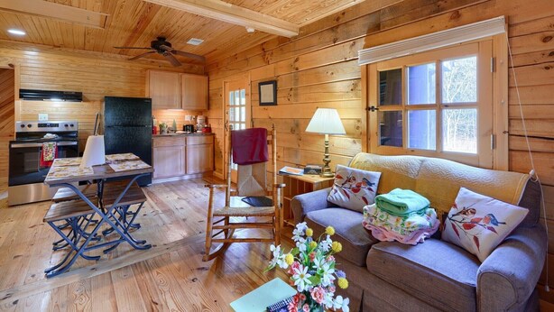 Een gezellig interieur van een chalet met een houten vloer, een eettafel, een schommelstoel, een bank en een keuken met een koelkast en fornuis.