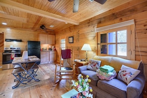Een gezellig interieur van een chalet met een houten vloer, een eettafel, een schommelstoel, een bank en een keuken met een koelkast en fornuis.
