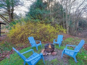 A fire pit with four blue chairs arranged around it in a wooded area. - Bison Hollow Hideaway (South Bloomingville)