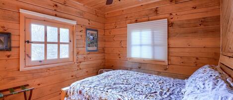 Un dormitorio de cabaña de madera con una cama, un ventilador de techo y dos ventanas.