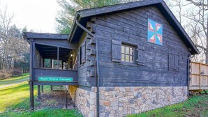 Une cabane rustique en bois, avec des fondations en pierre, un porche couvert et une enseigne indiquant qu’il s’agit de Bison Hollow Hideaway.