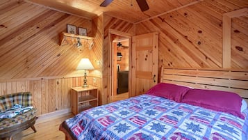 Een gezellig slaapkamer op zolder met een schuine houten balkenplafond, een bed met een kleurrijke quilt, een stoel en een tafeltje met een lamp.