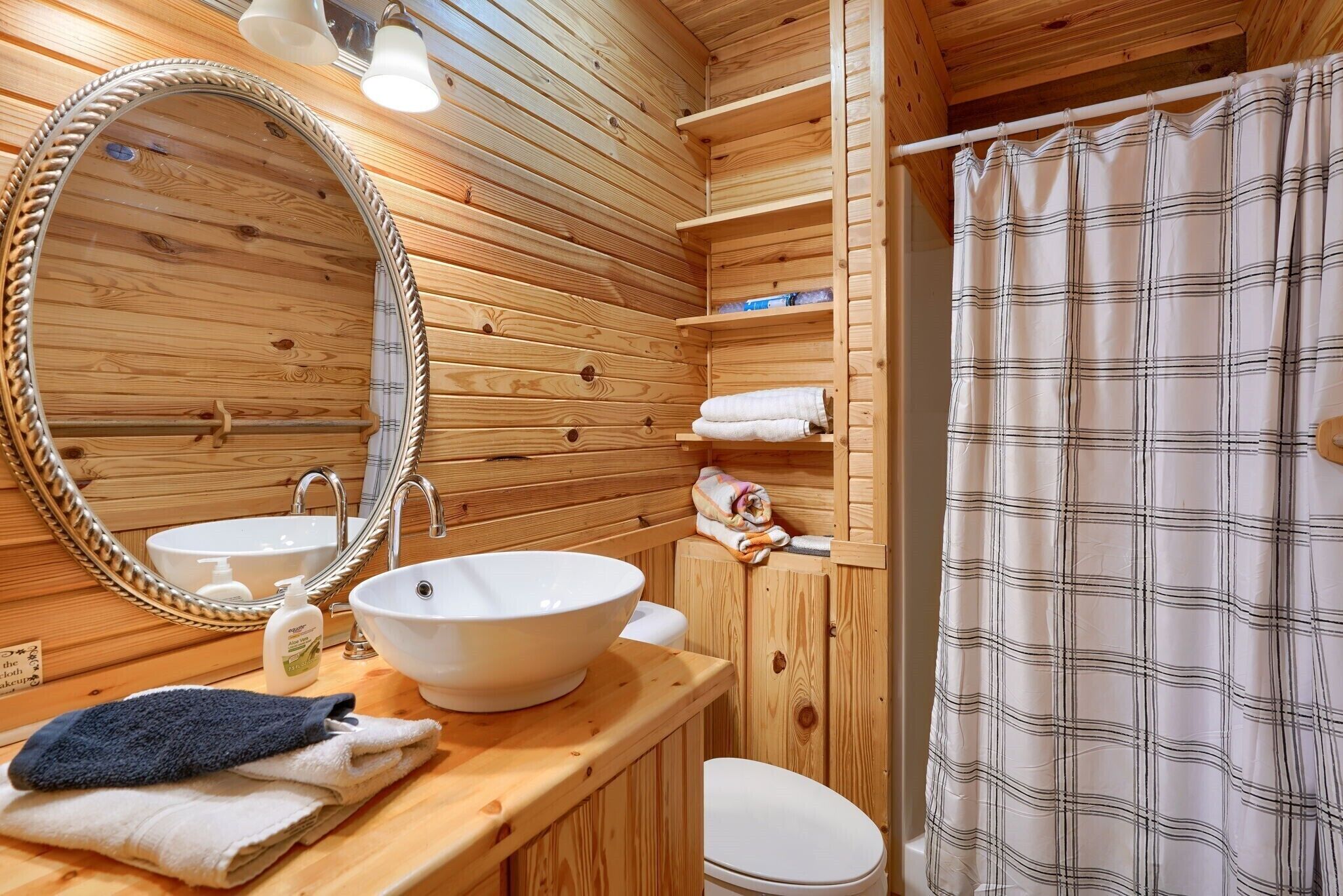 A wooden cabin bathroom with a round mirror, two sinks, a toilet, and a shower curtain.