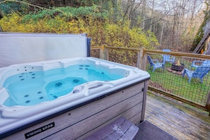 Un bain à remous sur une terrasse en bois, avec une rambarde en bois et une vue sur un jardin agrémenté d’arbres et d’arbustes.