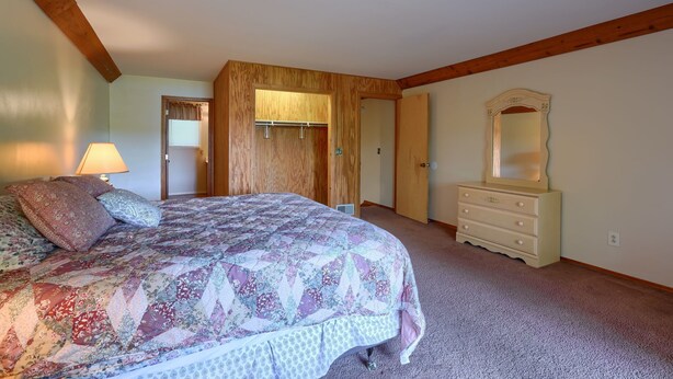 A bedroom with a large bed, a dresser, and a mirror. There is a door leading to another room.