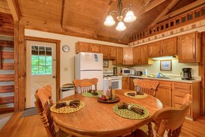 Interior de una cabaña de madera con una mesa de comedor dispuesta para cuatro personas, armarios de madera, un refrigerador y un microondas.
