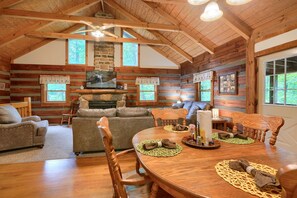 A log cabin interior with a fireplace, wooden furniture, and a dining table.