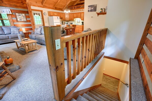 Ein gemütliches Blockhauss-Interieur mit einer Holztreppe, einem Wohnzimmer mit Sofa und Couchtisch sowie einer Küchenzeile.