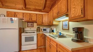 A kitchen with wooden cabinets, a white refrigerator, a stove, a microwave, a coffee maker, and a sink. - Chickasaw in Hocking Hills (Logan)