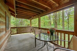 A wooden deck with a glass table and chairs, overlooking a forest.