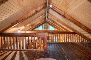 A wooden attic room with a sloped ceiling, a stone wall, and a wooden railing. - Cherokee in Hocking Hills (Logan)