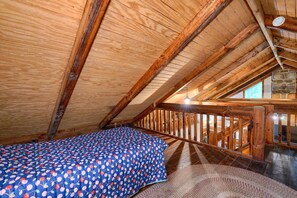 A bedroom with a wooden ceiling, a bed with a blue floral bedspread, and a stone fireplace.