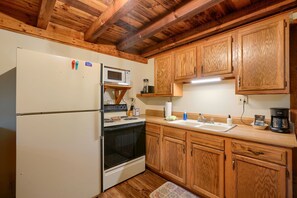 A kitchen with wooden cabinets, a white refrigerator, a microwave, a stove, and a coffee maker. - Cherokee in Hocking Hills (Logan)
