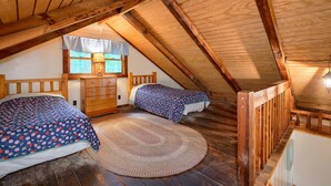 A cozy attic bedroom with two beds, a wooden ceiling, and a large window. - Cherokee in Hocking Hills (Logan)