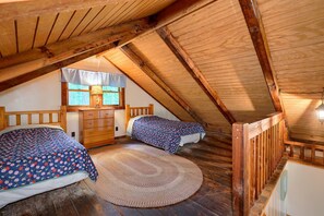 A cozy attic bedroom with two beds, a wooden ceiling, and a large window.