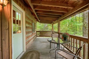 A wooden porch with a glass table and benches, overlooking a forested area.