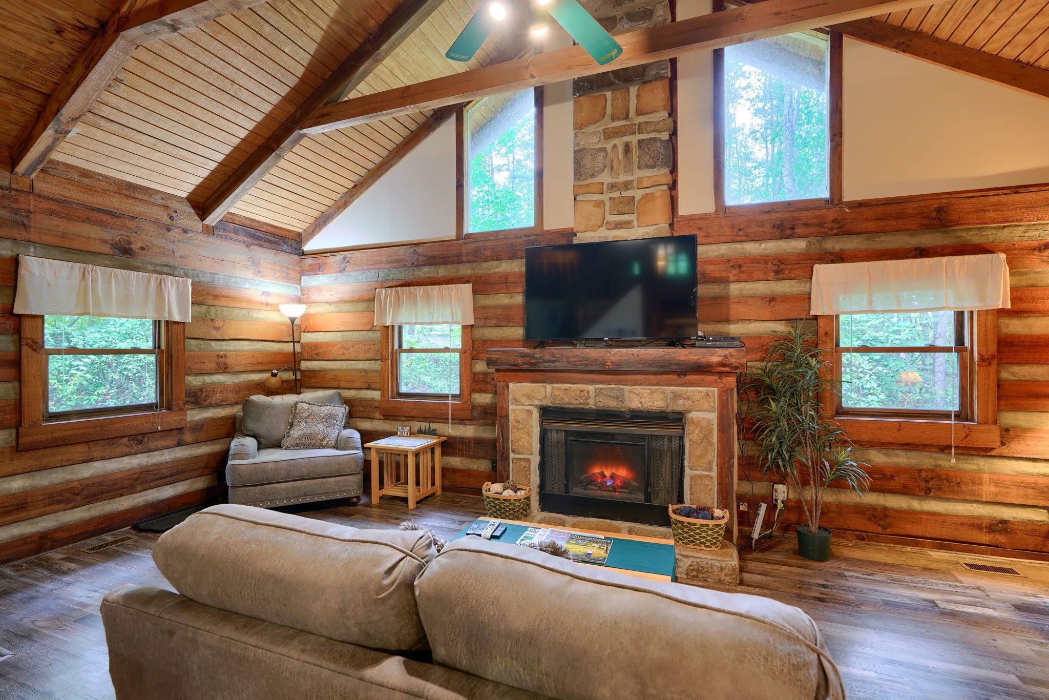 A log cabin interior with a fireplace, a television, and a cozy seating area.