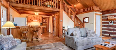 A spacious living area with a wooden staircase, a kitchen with wooden cabinets, and a cozy seating area with a sofa and chairs.