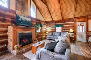 A log cabin interior with a fireplace, wooden walls, a sofa, and a dining area.
