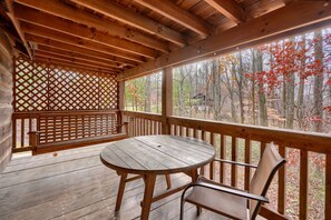 A wooden deck with a round table and chairs, a lattice screen, and a view of a forest with autumn foliage. - Shawnee in Hocking Hills (Logan)